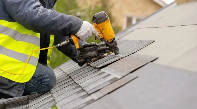 roofer using nail gun to install shingles